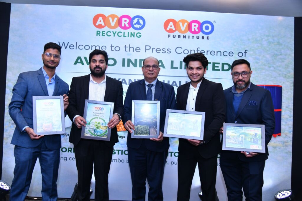Five senior leaders of AVRO stand on stage at a press conference, each holding framed sustainability or corporate achievement certificates. The backdrop displays the AVRO Recycling and AVRO Furniture logos along with the text “Welcome to the Press Conference of AVRO INDIA LIMITED.” The leaders are dressed in formal business suits, posing confidently in a well-lit corporate event setting.